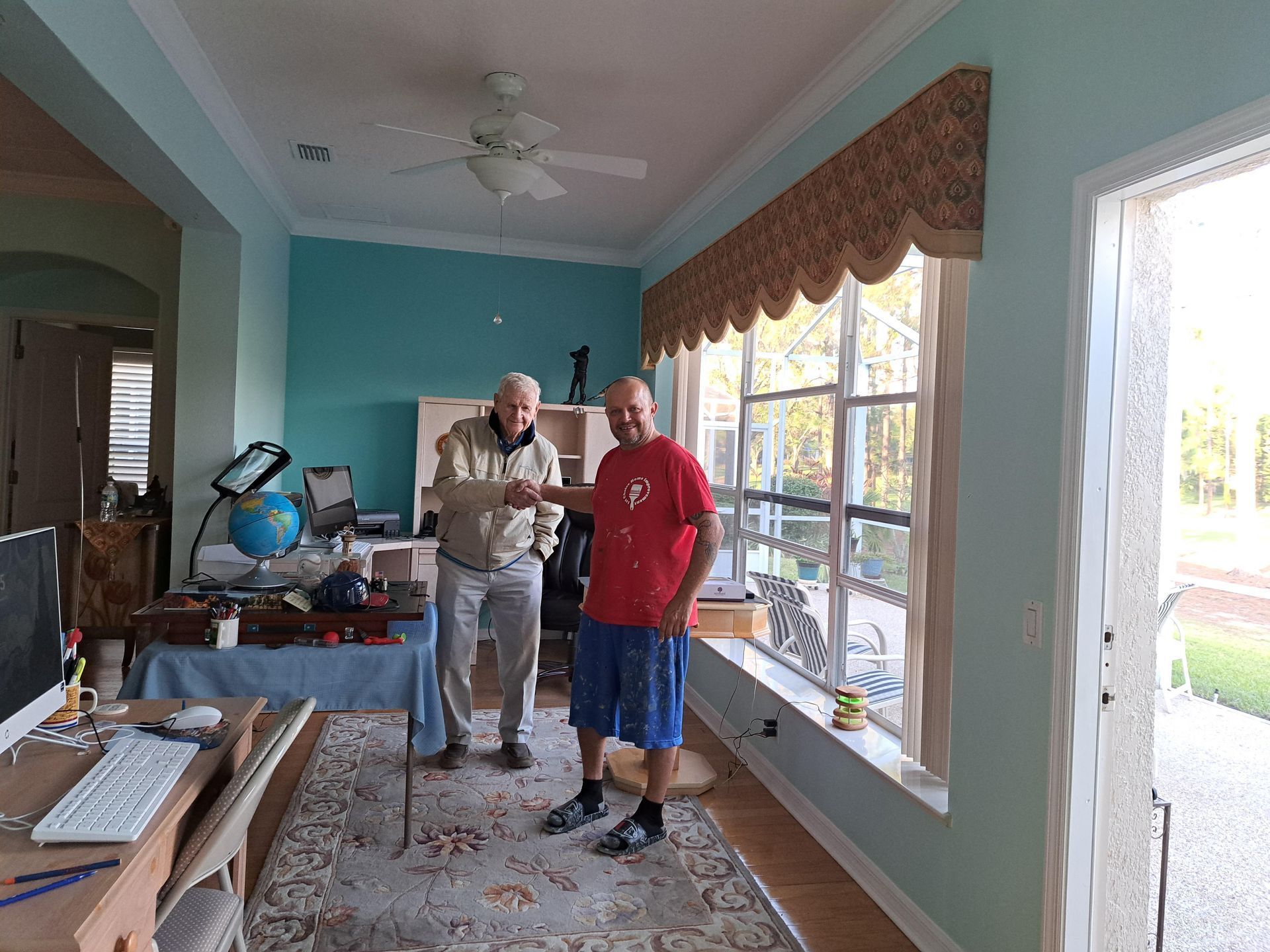 Two men are standing in a living room in front of a window.