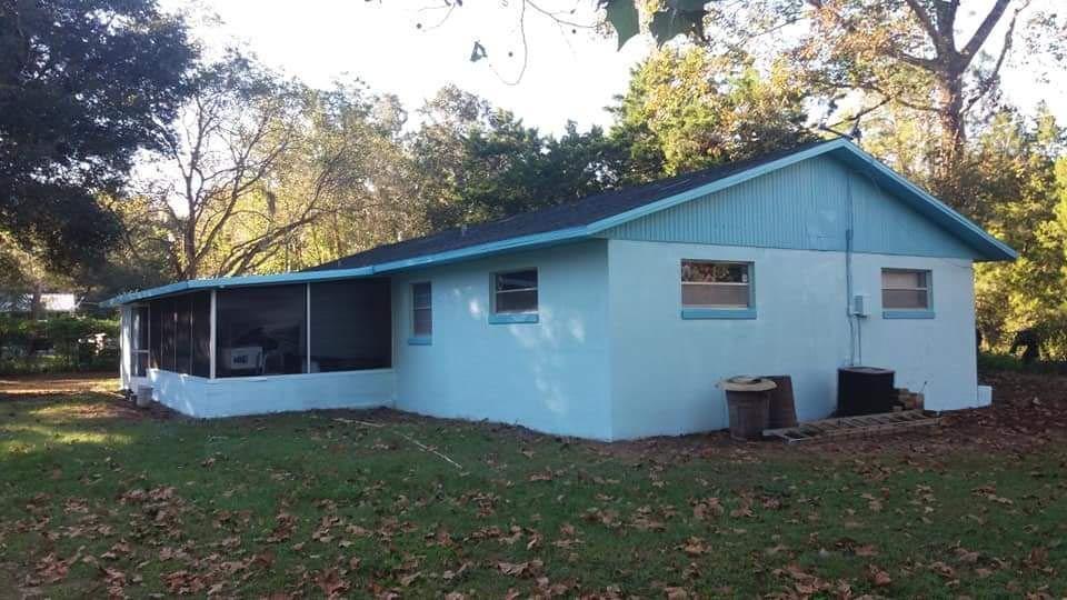 A blue house with a screened in porch and trees in the background