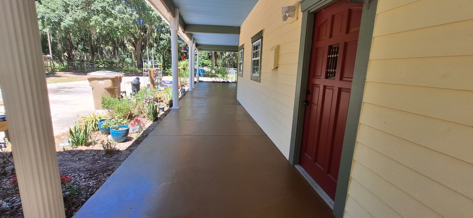 A long porch leading to a red door of a house.