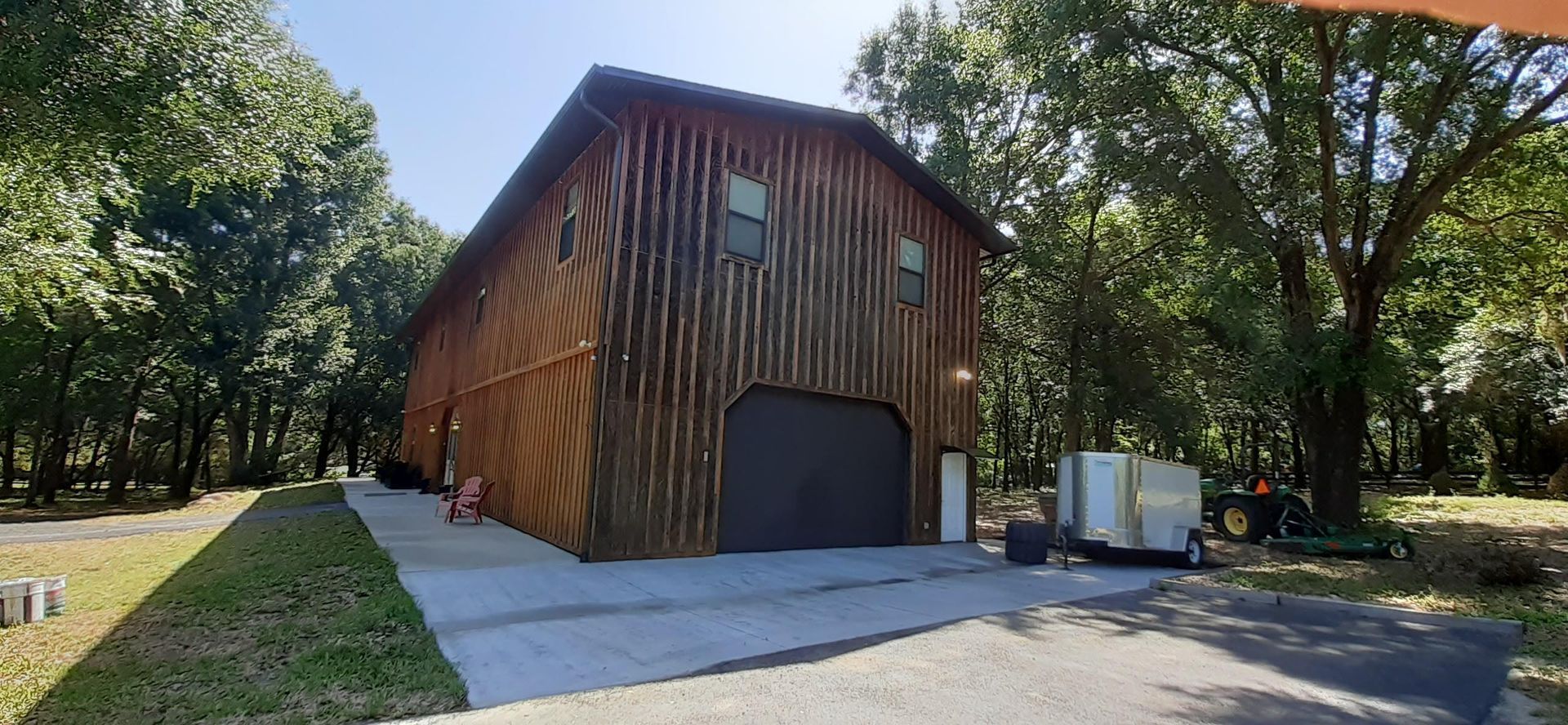 A large wooden barn with a black garage door is surrounded by trees.