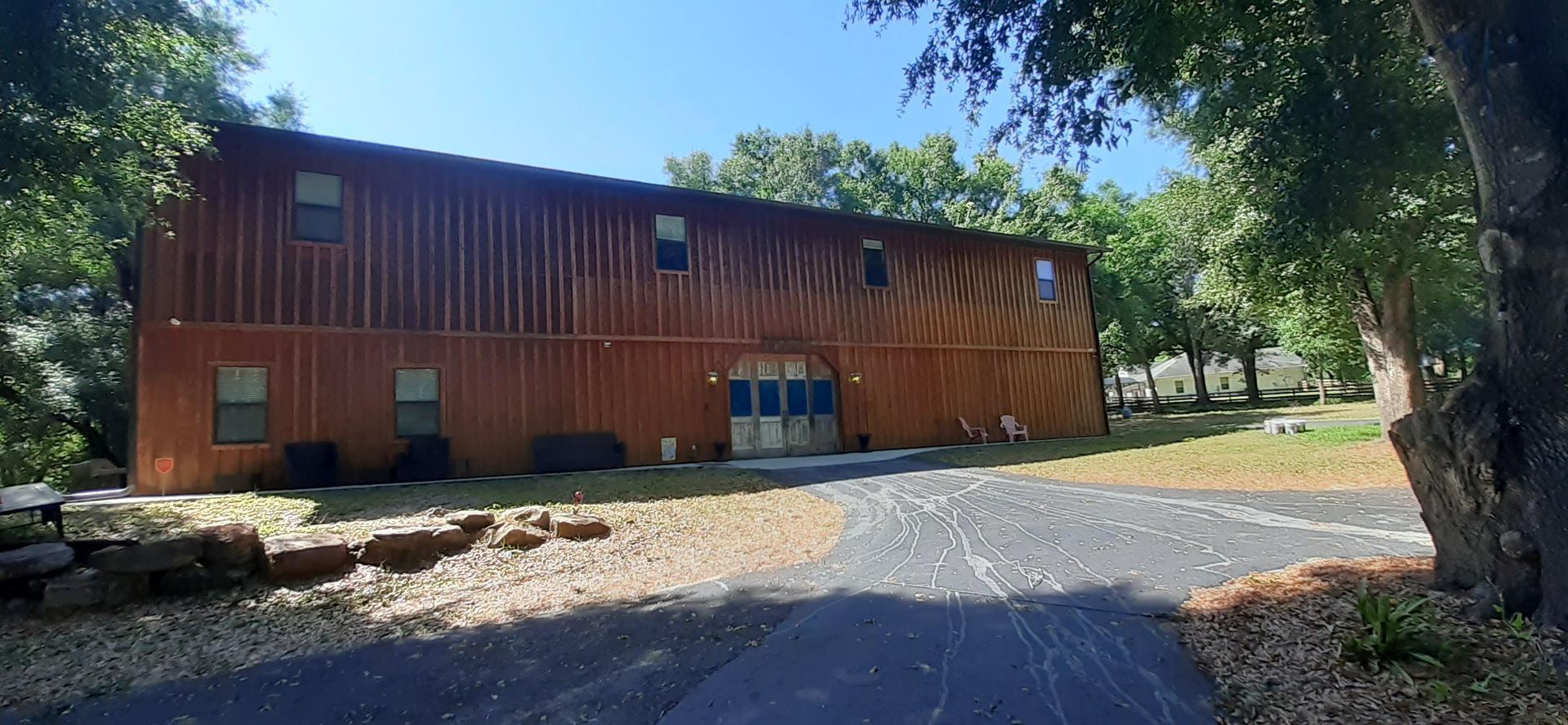 A large wooden building with a driveway leading to it is surrounded by trees.
