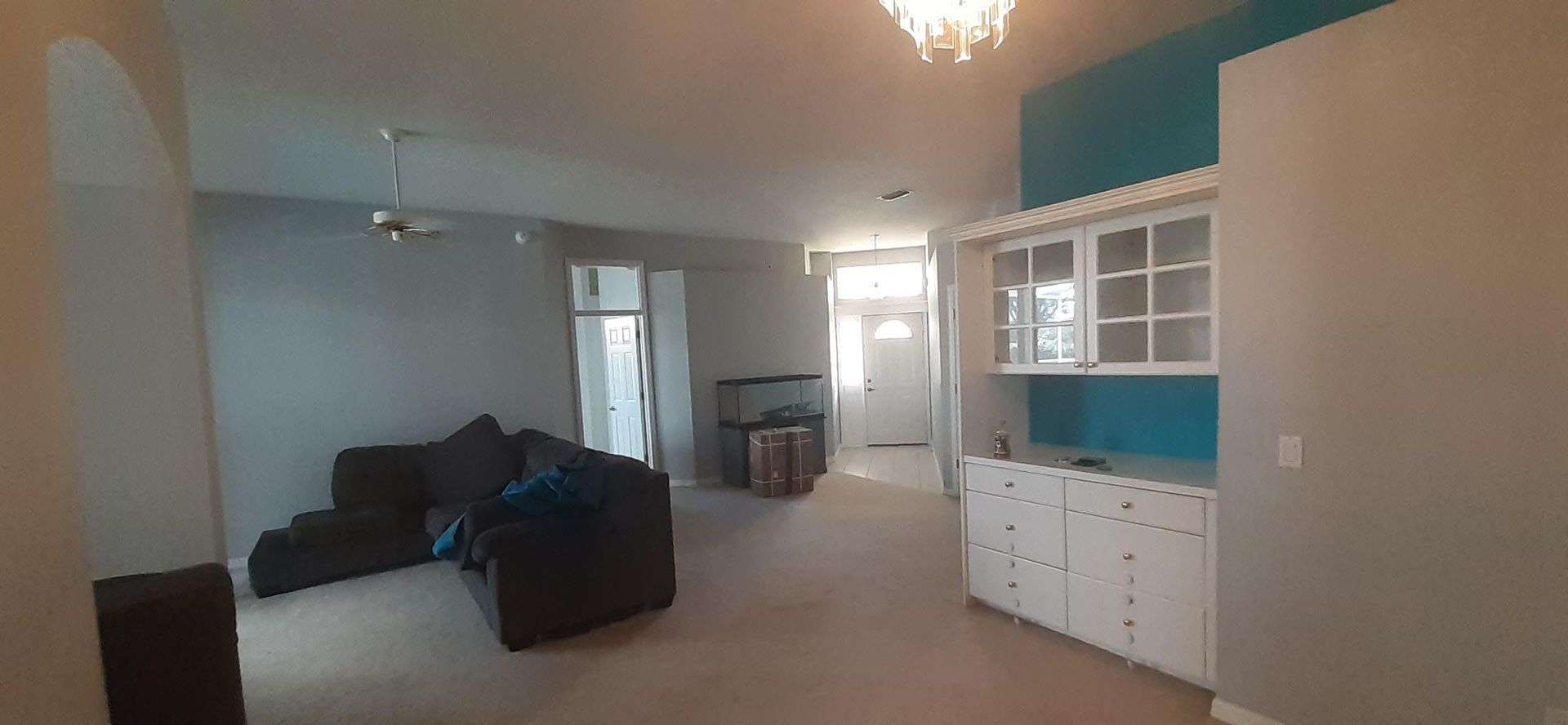A living room with a couch , chairs , cabinets and a chandelier.