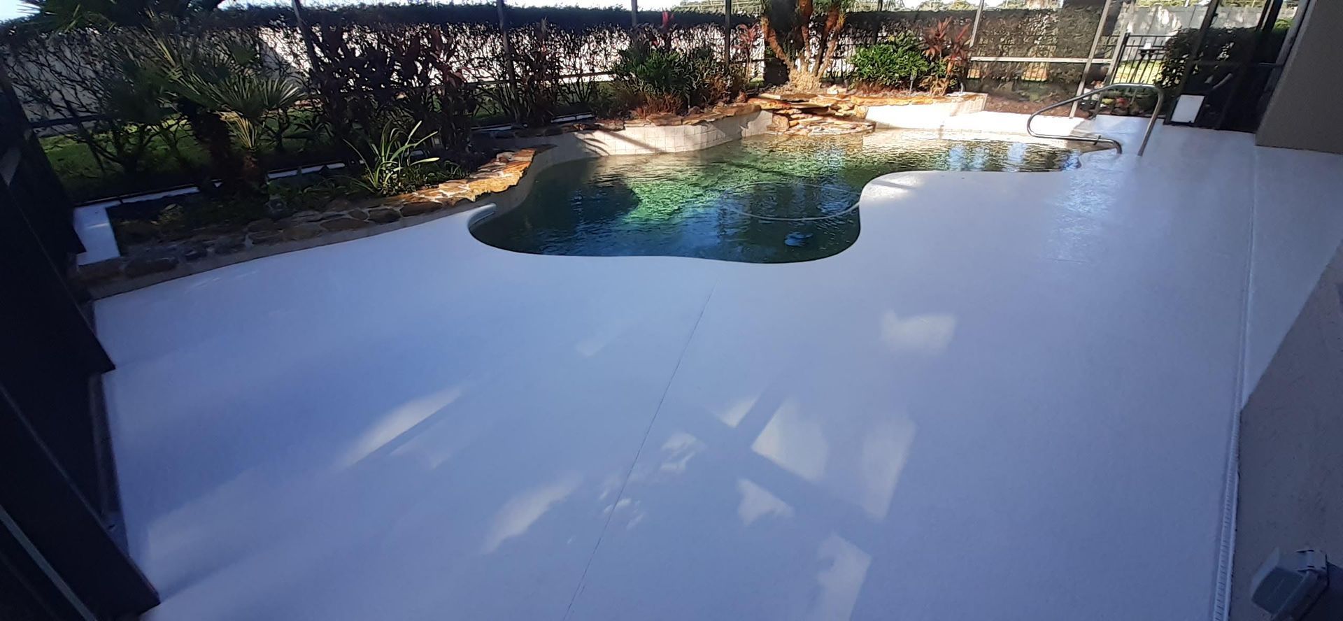 A white patio with a swimming pool in the background.