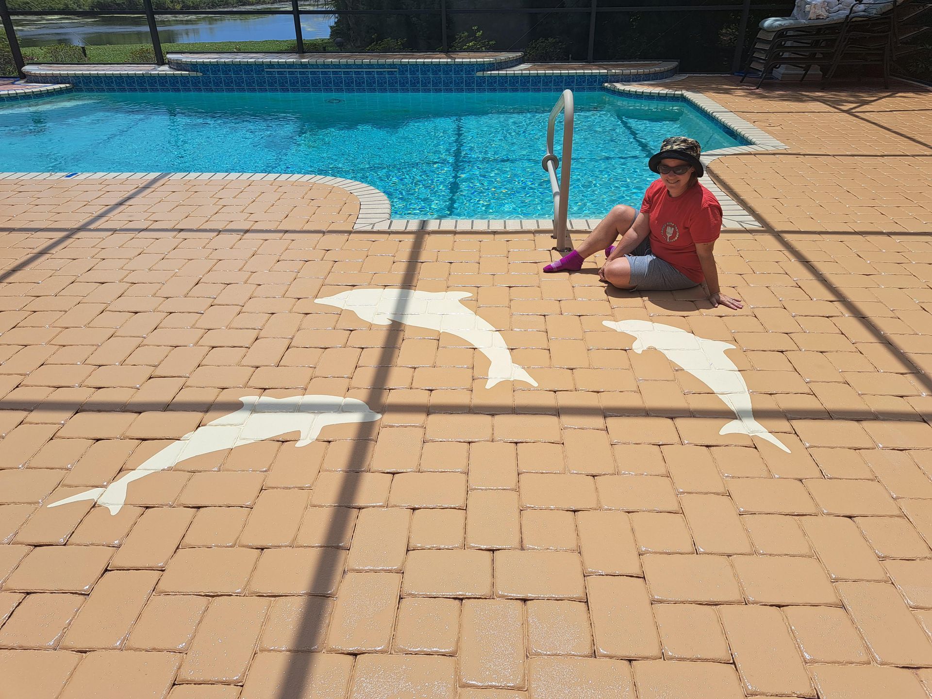A woman is sitting on the ground next to a swimming pool with dolphins painted on the ground.