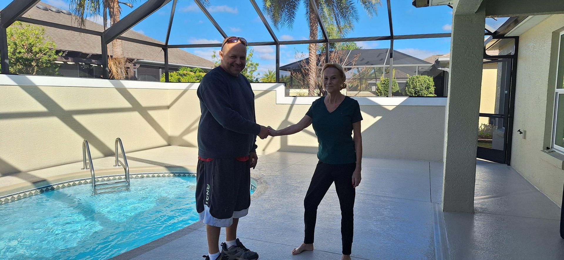 A man and a woman are shaking hands in front of a swimming pool.