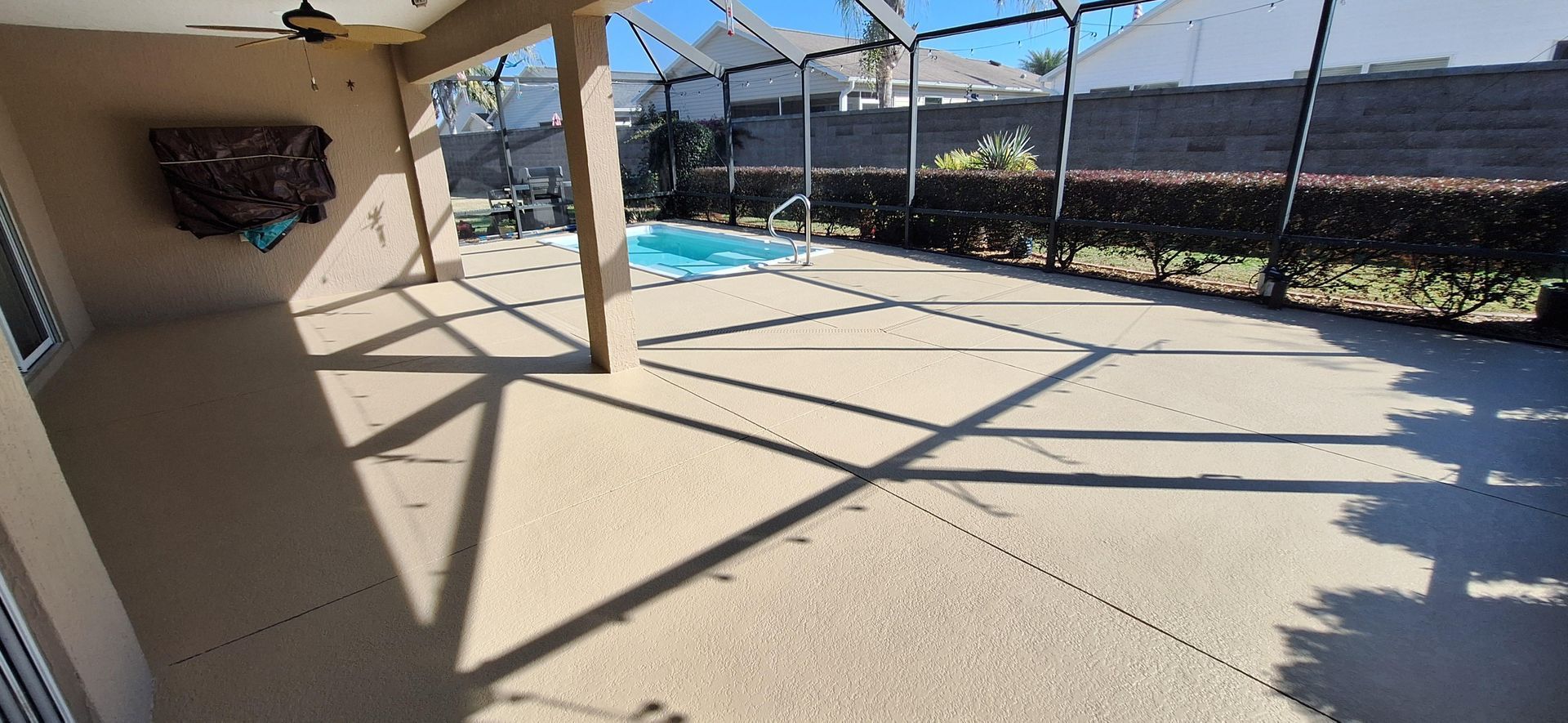A patio with a screened in pool and a ceiling fan.