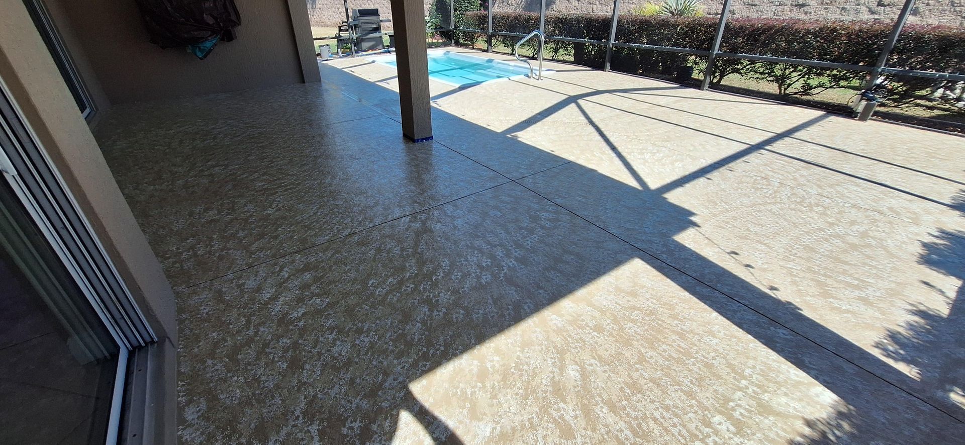 A patio with a sliding glass door and a pool in the background.