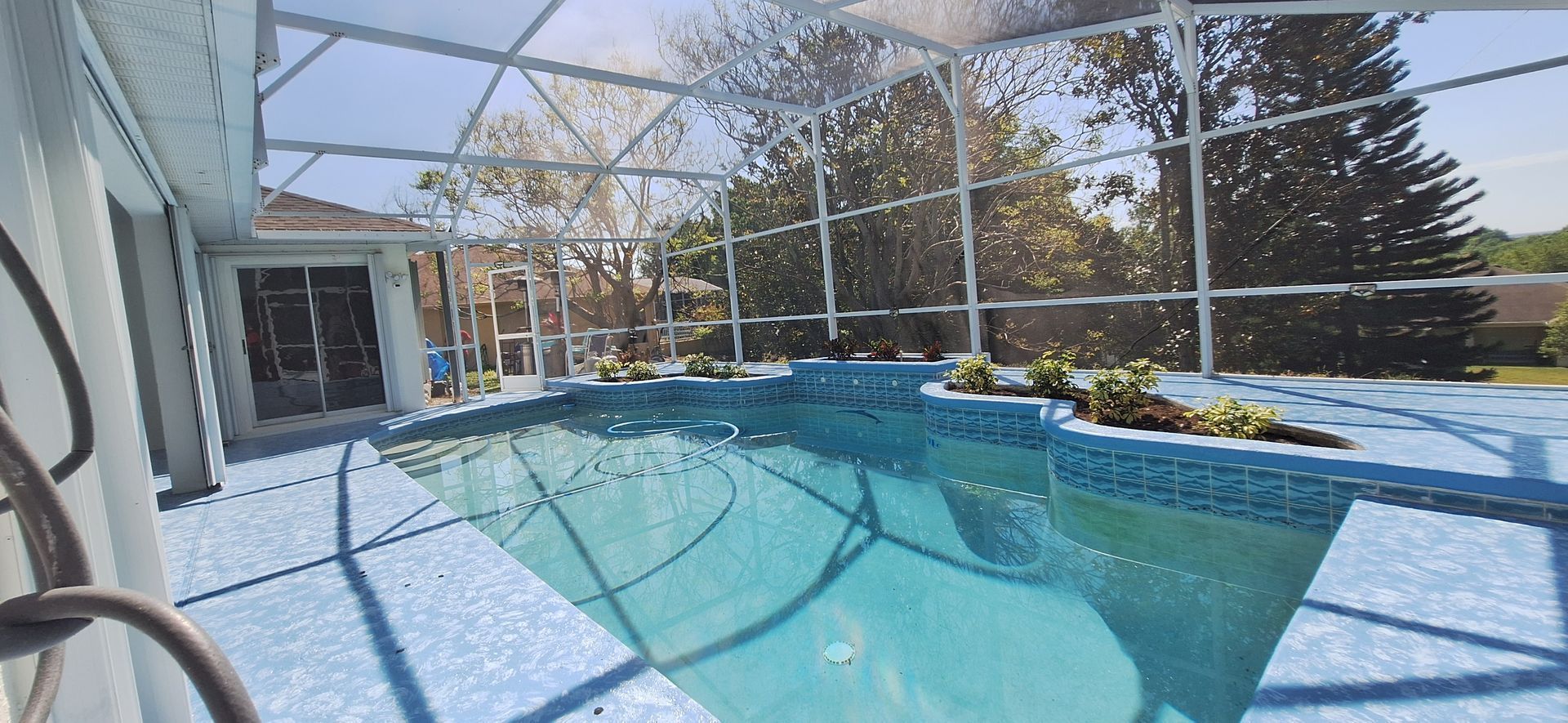 A large swimming pool is surrounded by a screened in area.