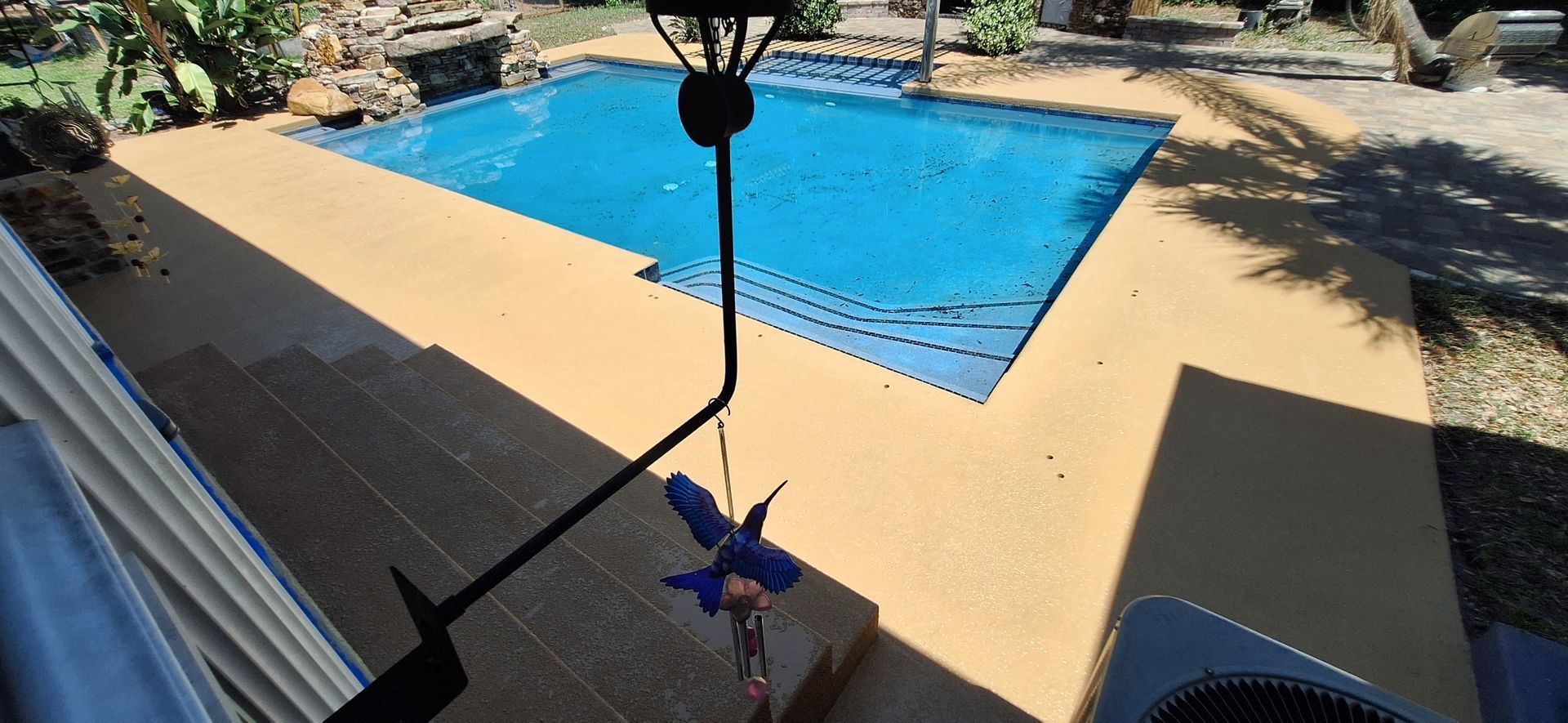 A large swimming pool is surrounded by a patio and a bird feeder.