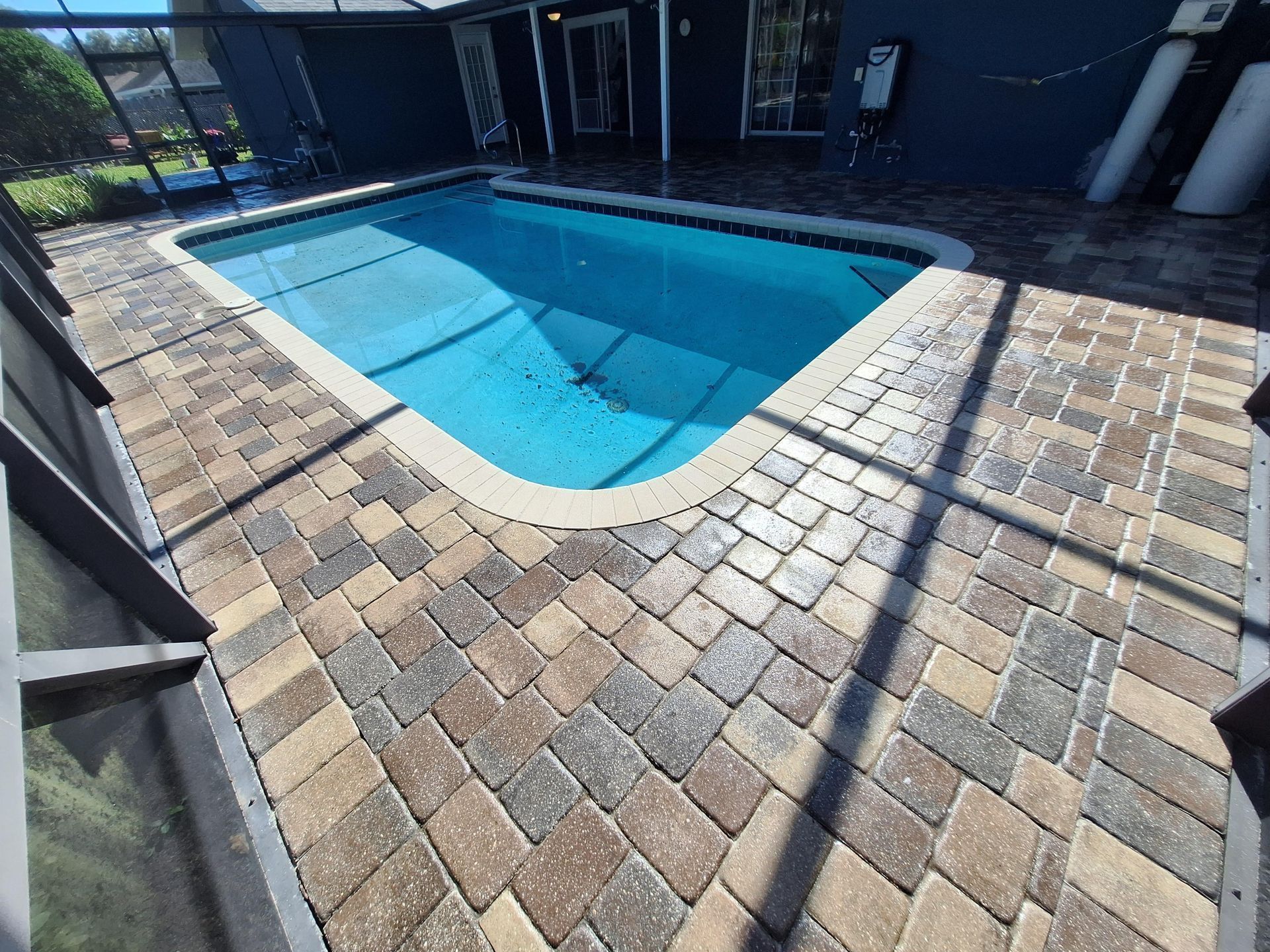 A large swimming pool is surrounded by bricks and a screened in area.