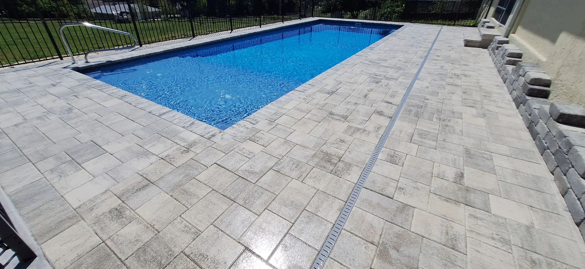A large swimming pool is surrounded by a brick patio.