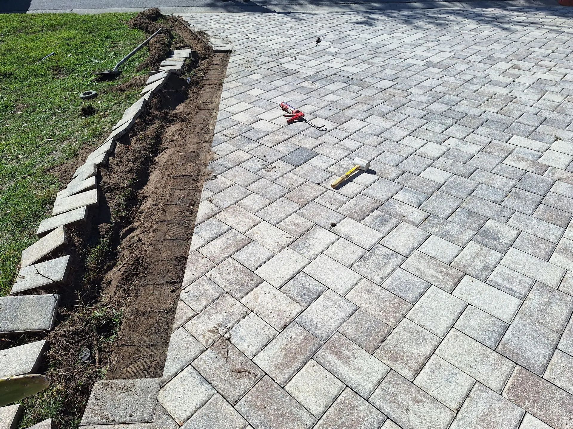 A brick driveway is being built next to a grassy area.