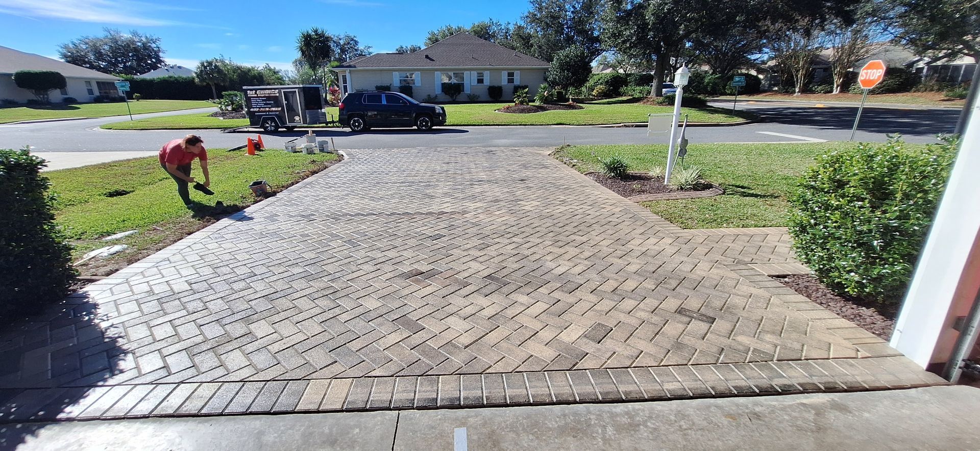 A man is working on a brick driveway in front of a house.