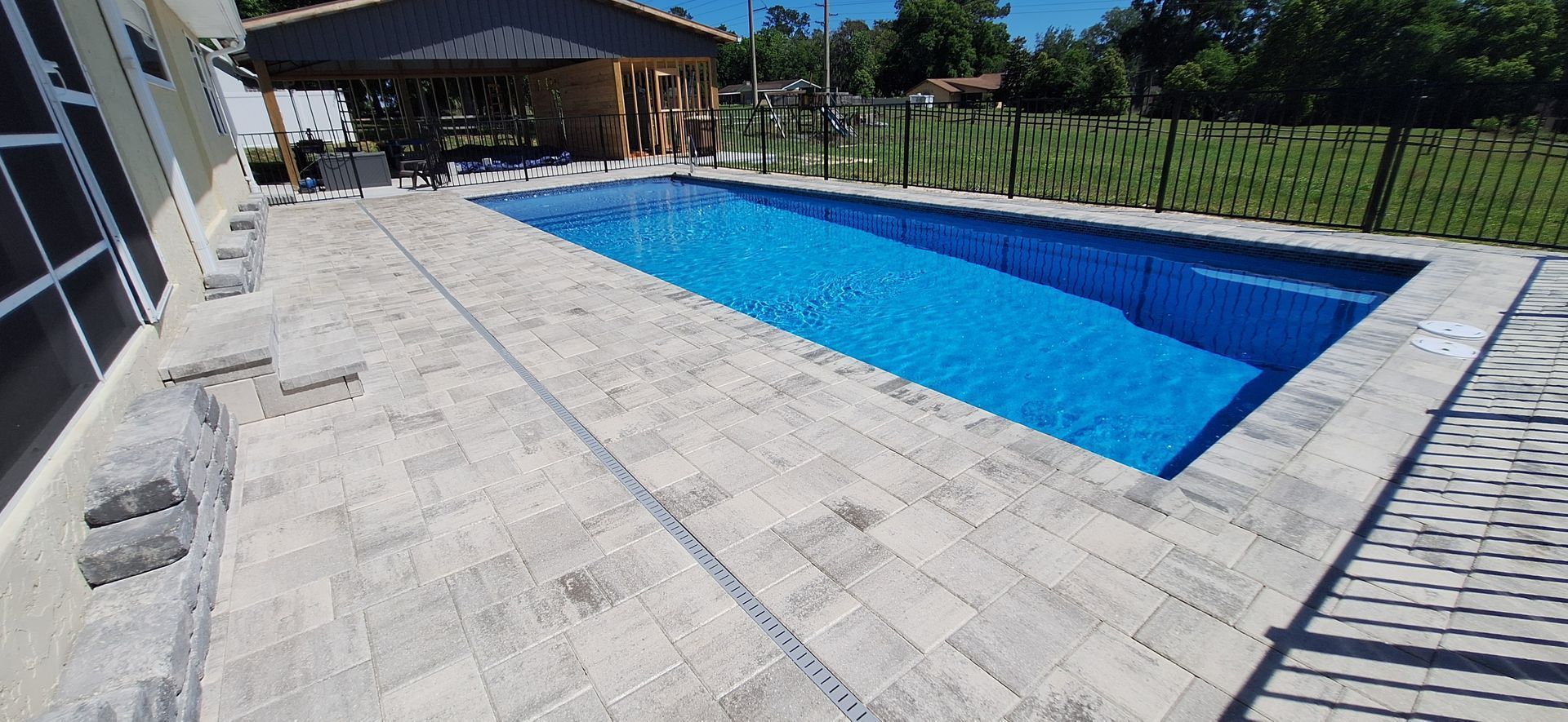 A large swimming pool is surrounded by a brick patio.