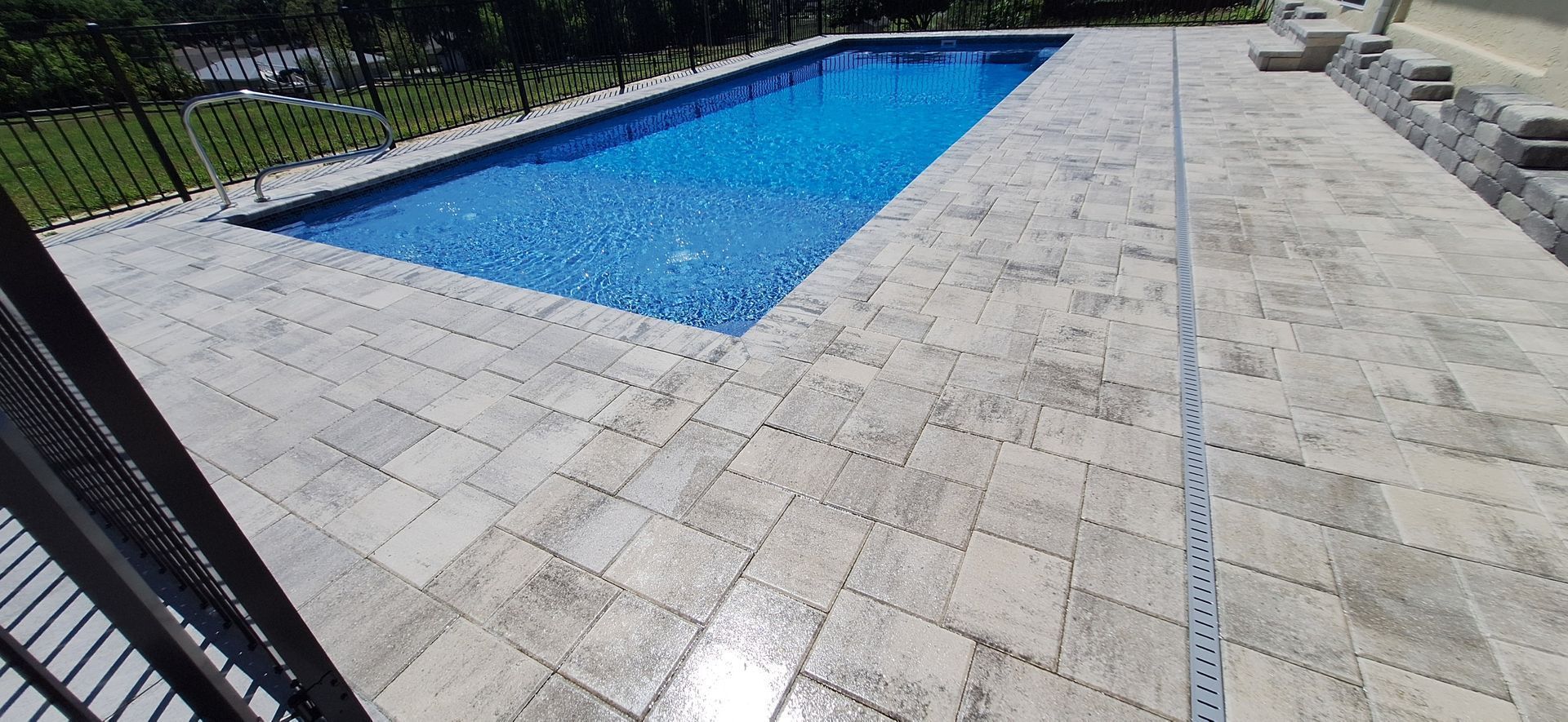 A large swimming pool is surrounded by a tiled patio.