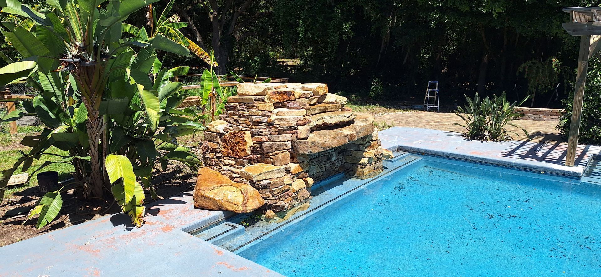 A large swimming pool surrounded by trees and rocks in a backyard.