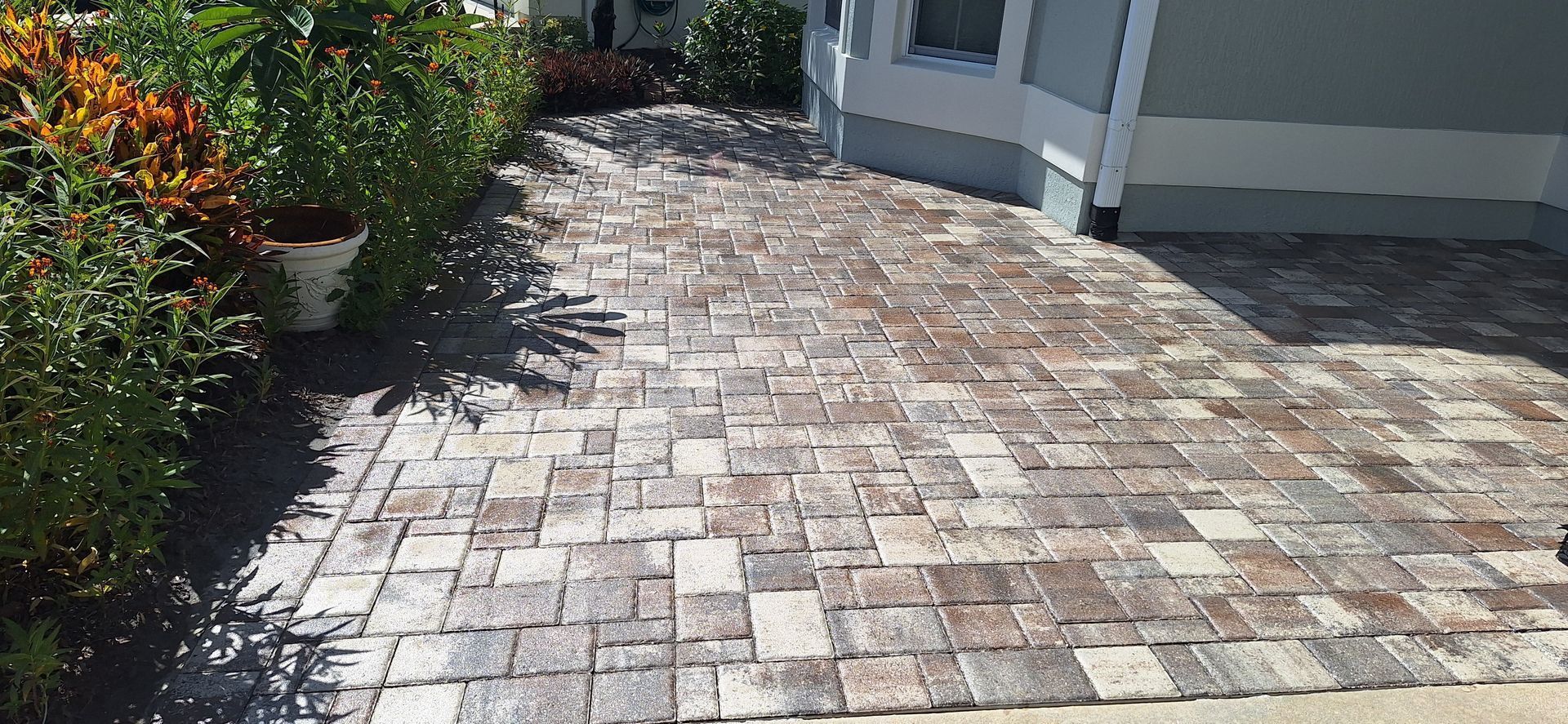 A brick walkway leading to a house with potted plants on the side.