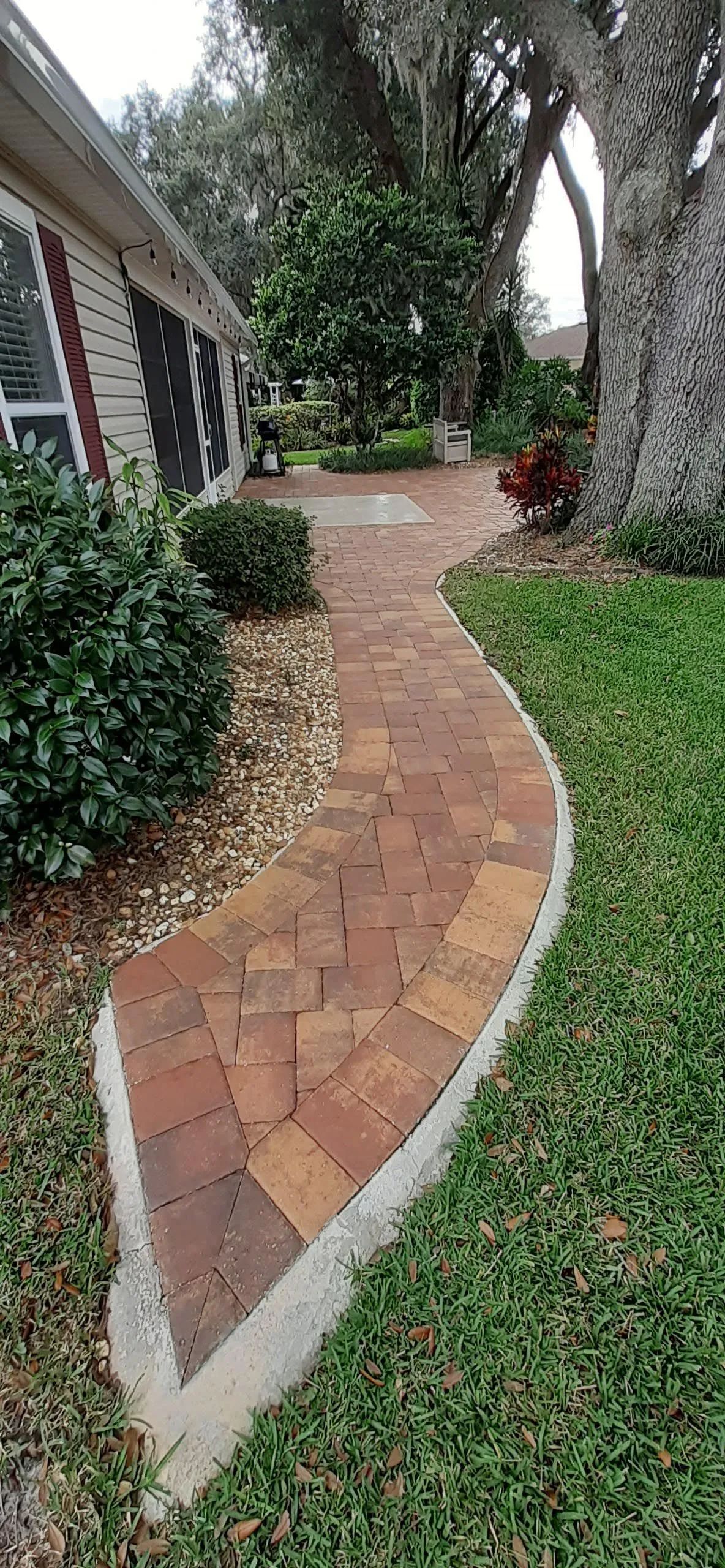 A brick walkway leading to a house surrounded by grass and trees.