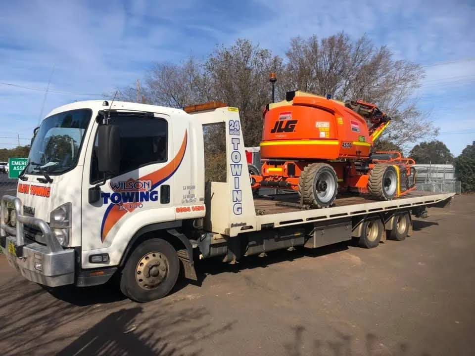 Wilson Towing truck in Dubbo transporting a large orange boom lift on a tilt tray