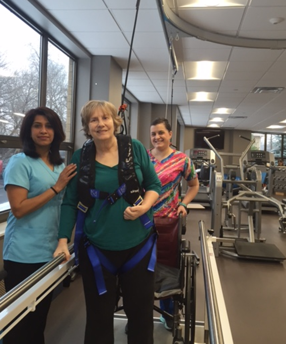 Woman learning to walk with the help of physical therapists and a walking harness.