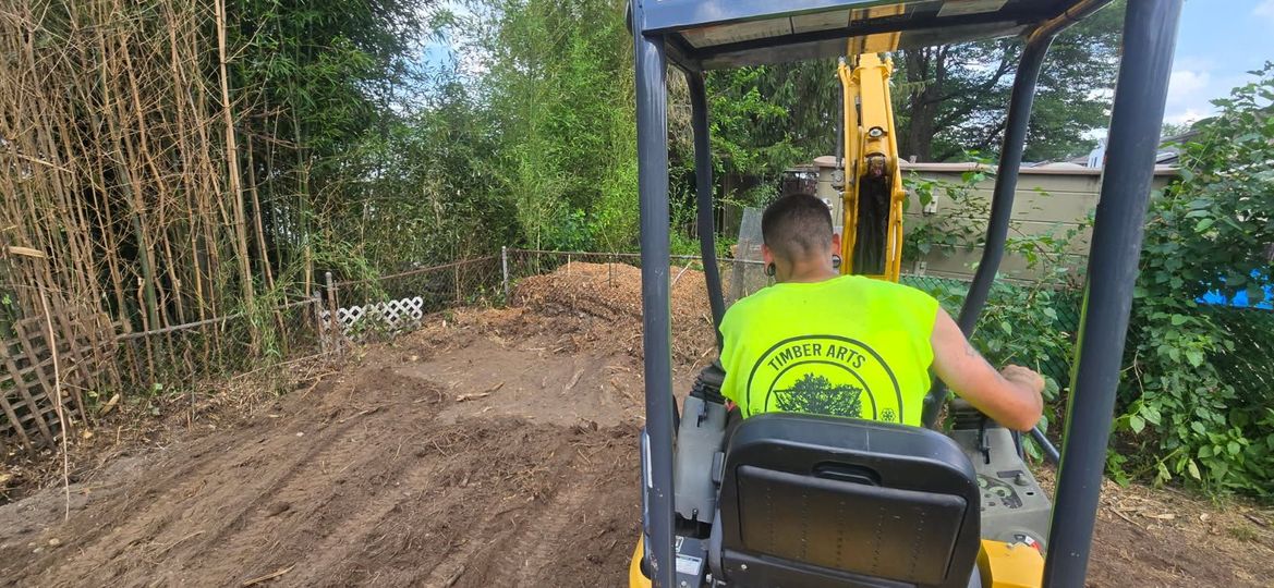 Person operating a yellow excavator. They are wearing a neon yellow shirt. They are working on a dirt pile.