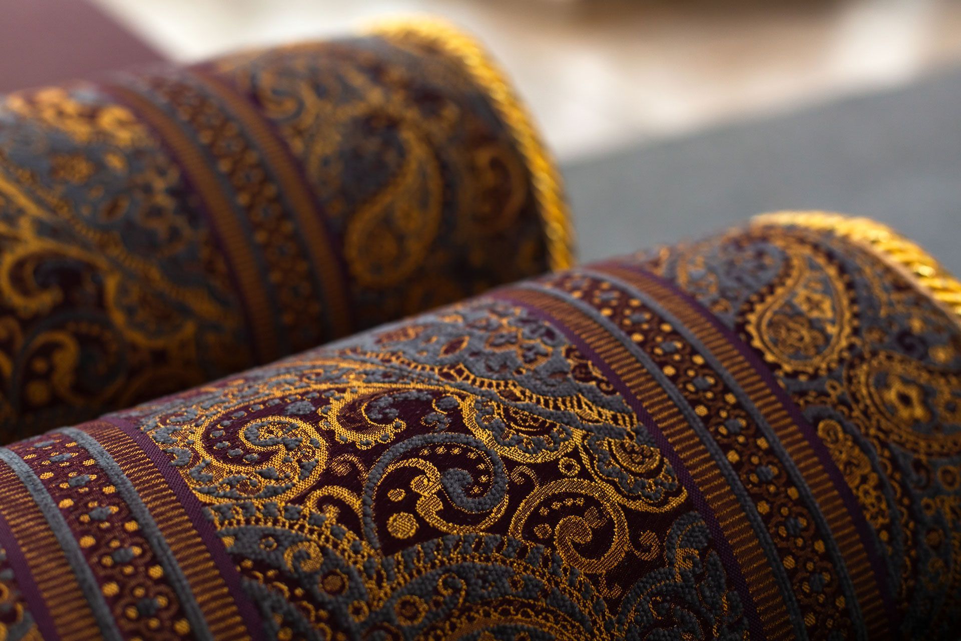 Two ornate rolled prayer rugs in dark purple and gold patterned fabric