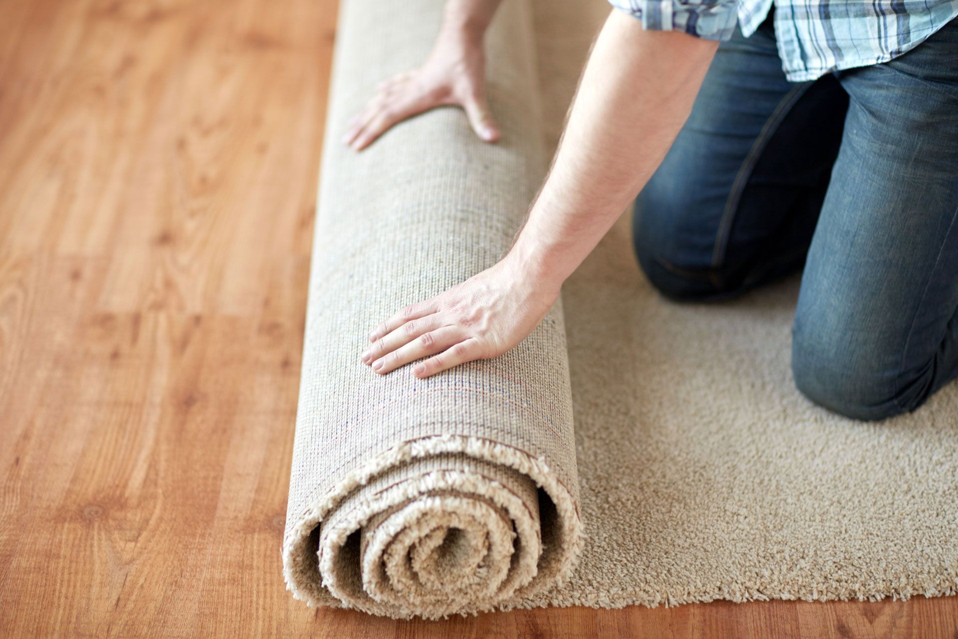 Person rolling up a beige carpet on a hardwood floor