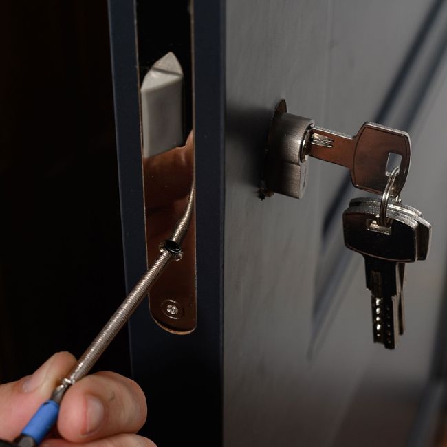 A person is fixing a door lock with a screwdriver