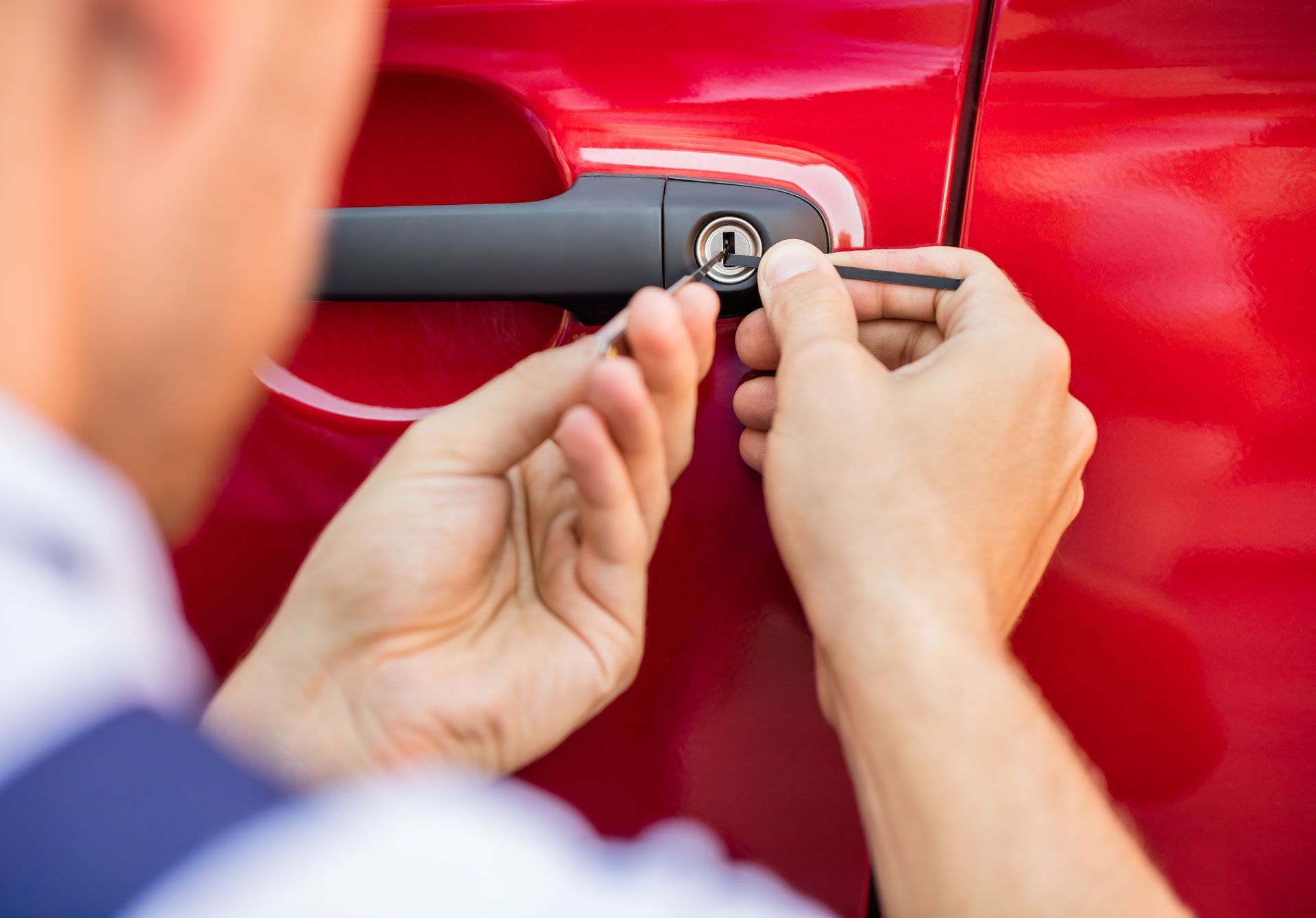 A man is using a screwdriver to open the door of a red car.