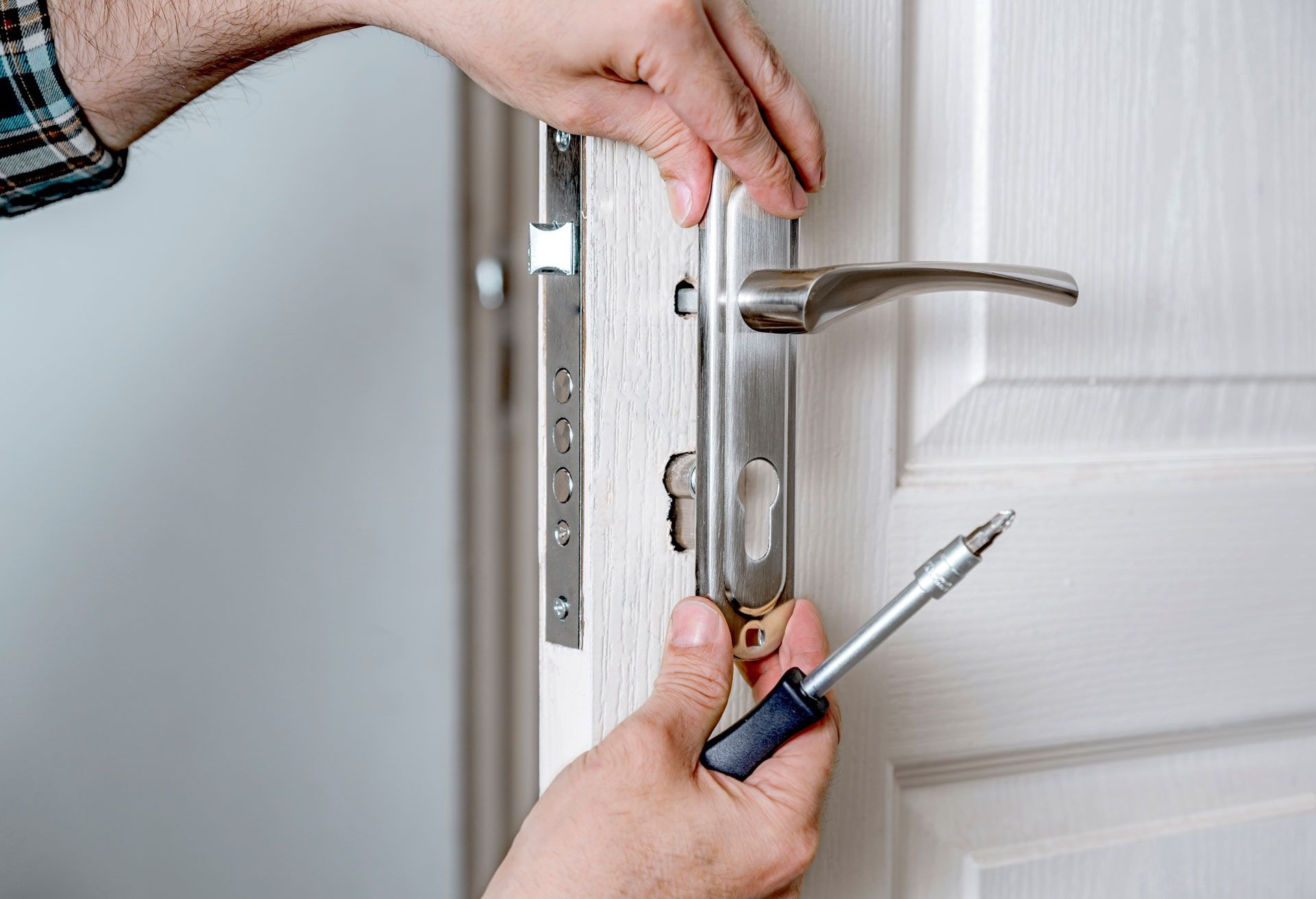 A man is fixing a door lock with a screwdriver.