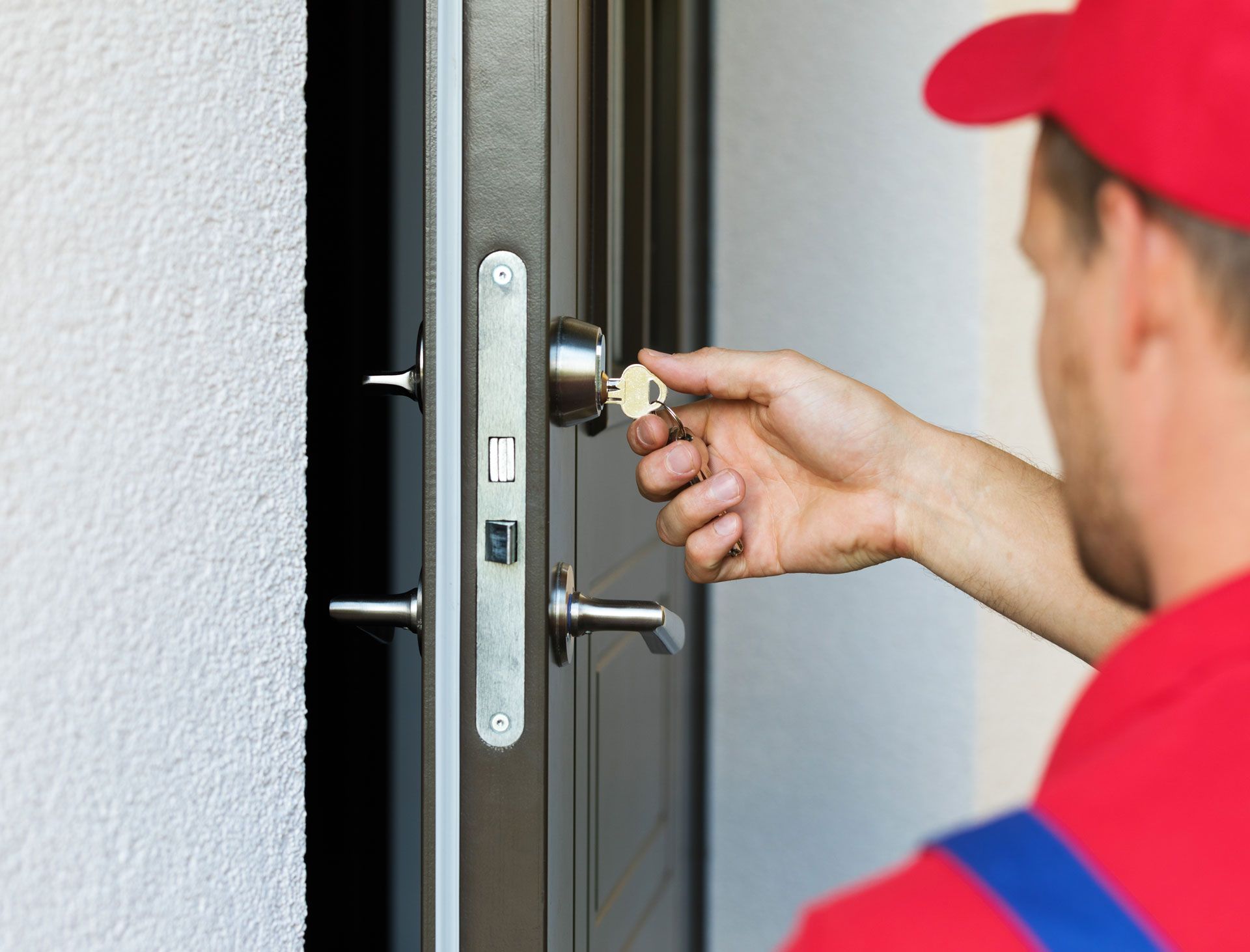 A man in a red hat is opening a door with a key.
