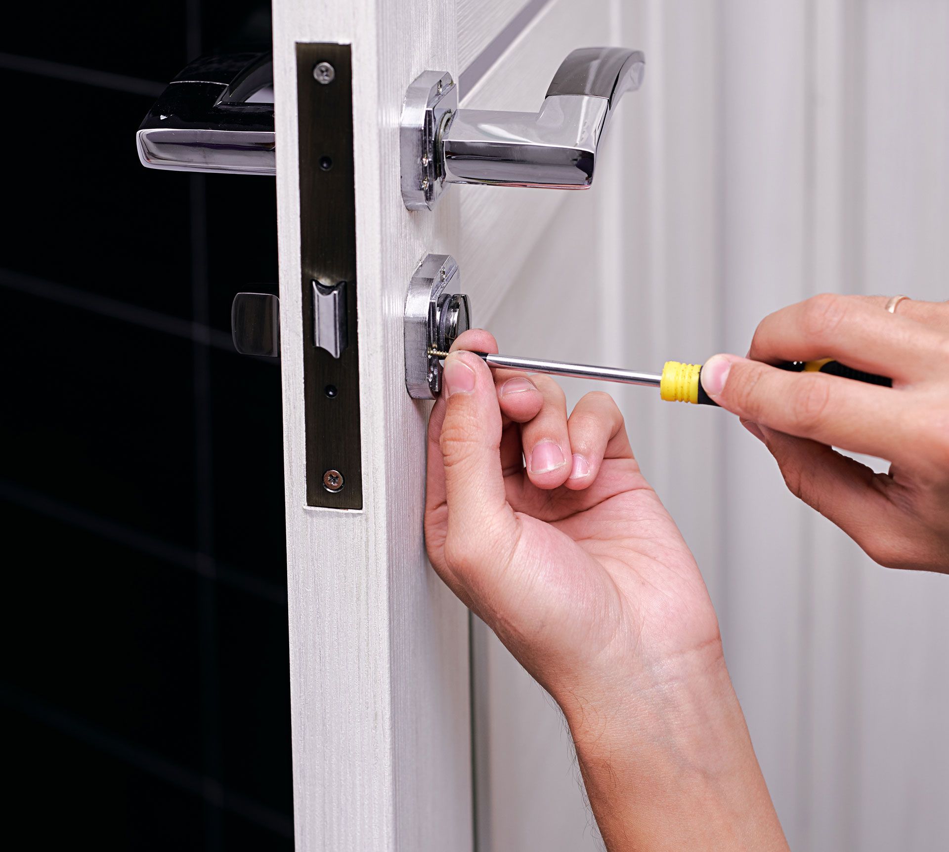 A person is fixing a door handle with a screwdriver.