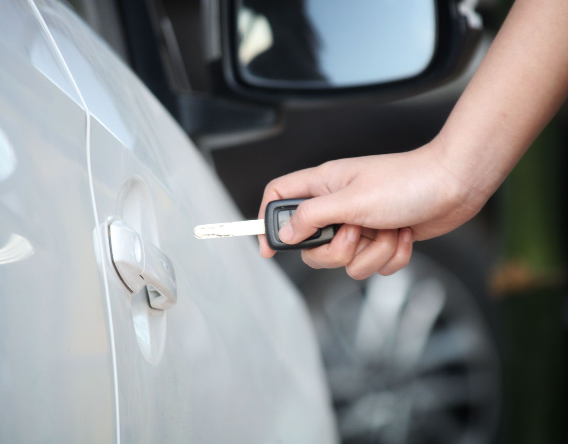 A person is holding a car key in front of a car door.
