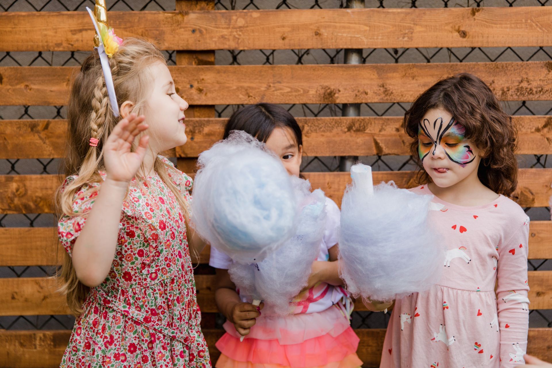 Three little girls are eating cotton candy in front of a wooden wall.