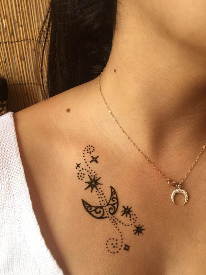 A woman has a tattoo of a crescent moon and stars on her chest