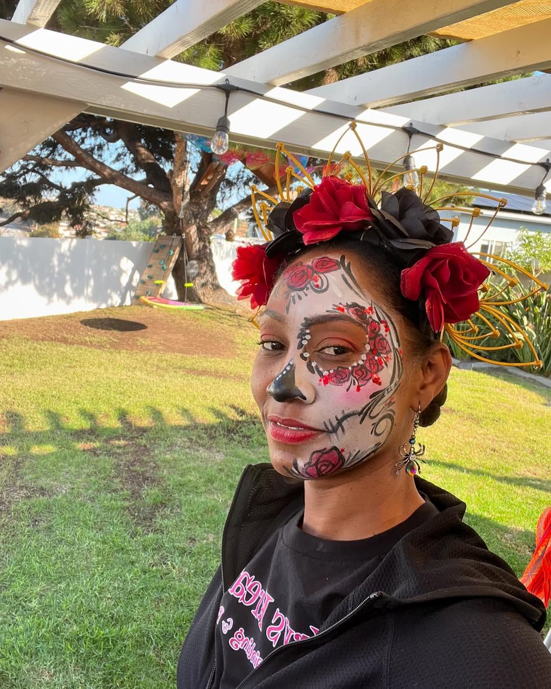 A woman with sugar skull makeup on her face is wearing a flower crown.