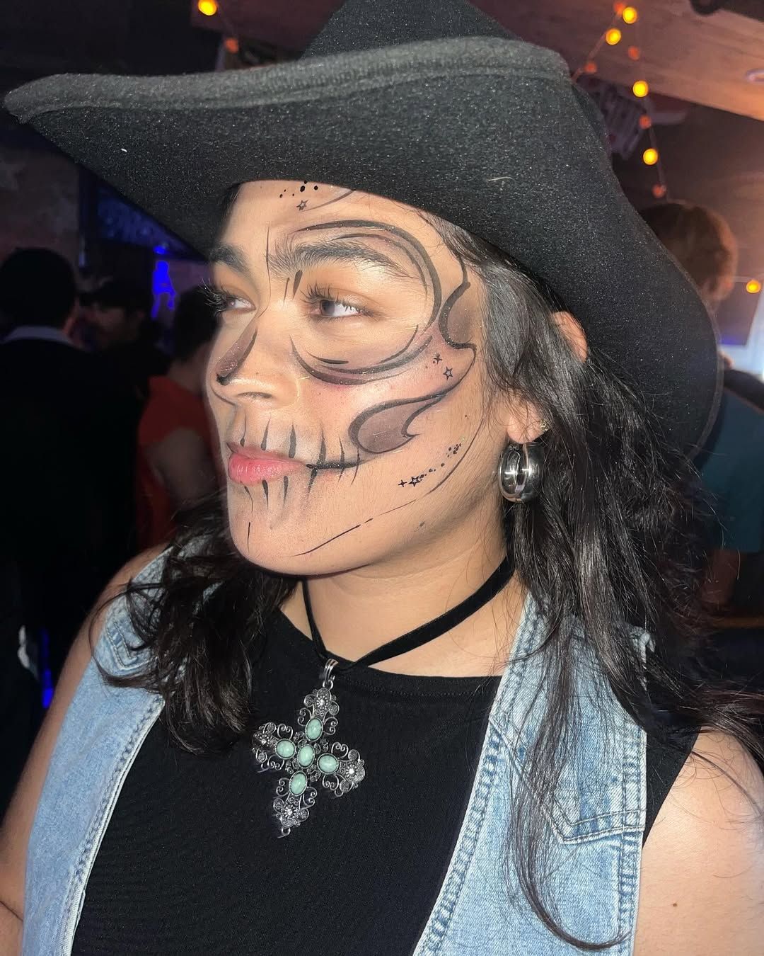A woman wearing a cowboy hat has a skull painted on her face