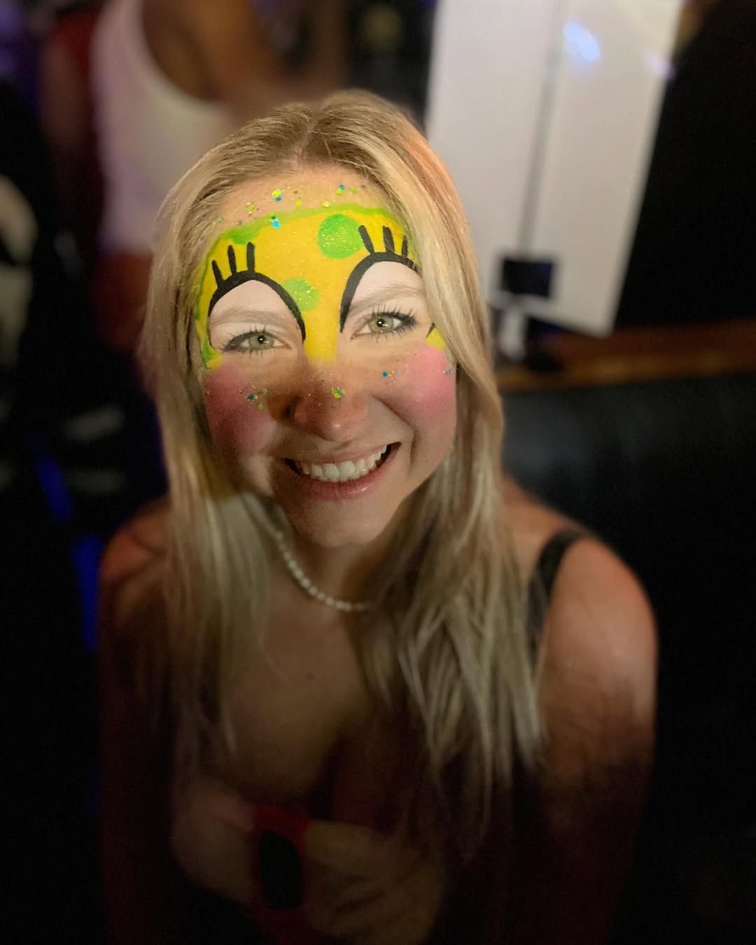 A woman with spongebob painted on her face is smiling.