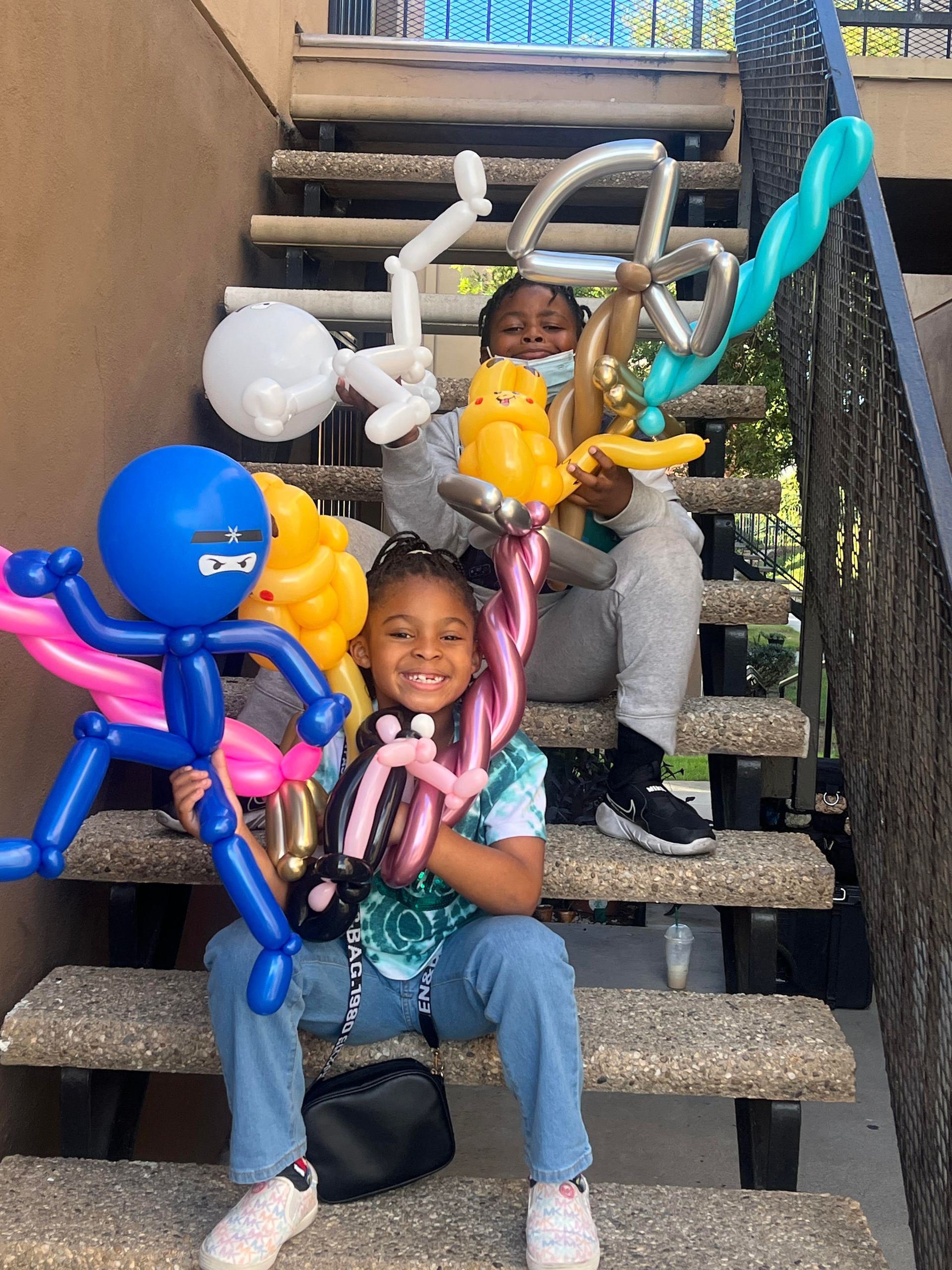 Two children are sitting on a set of stairs holding balloons.