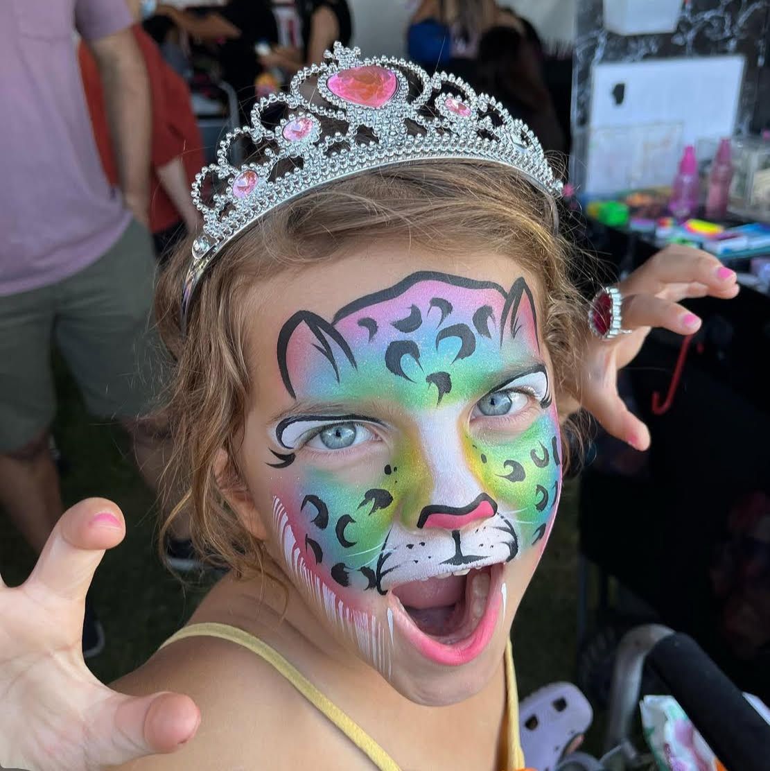 A little girl with her face painted like a leopard and wearing a tiara