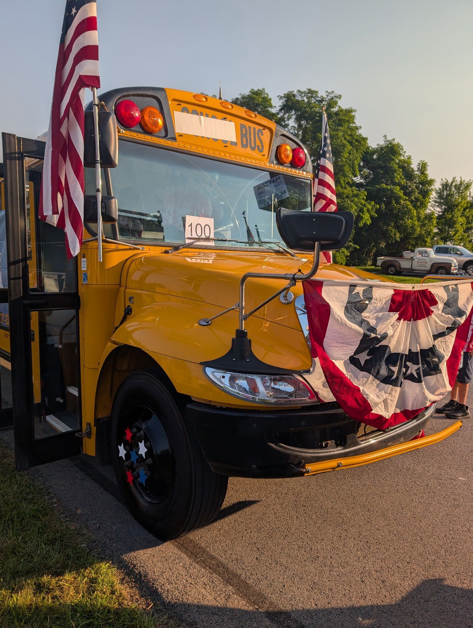 Yellow school bus decorated with patriotic bunting and flags, parked outdoors in sunlight