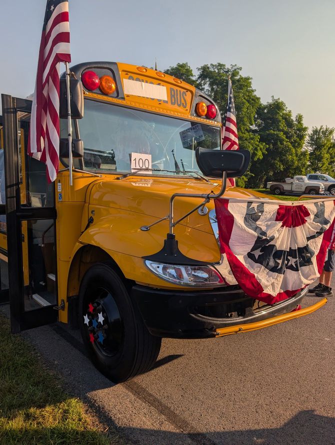 Yellow school bus decorated with patriotic bunting and flags, parked outdoors in sunlight