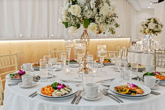 A table set for a wedding reception with plates of food and a vase of flowers.