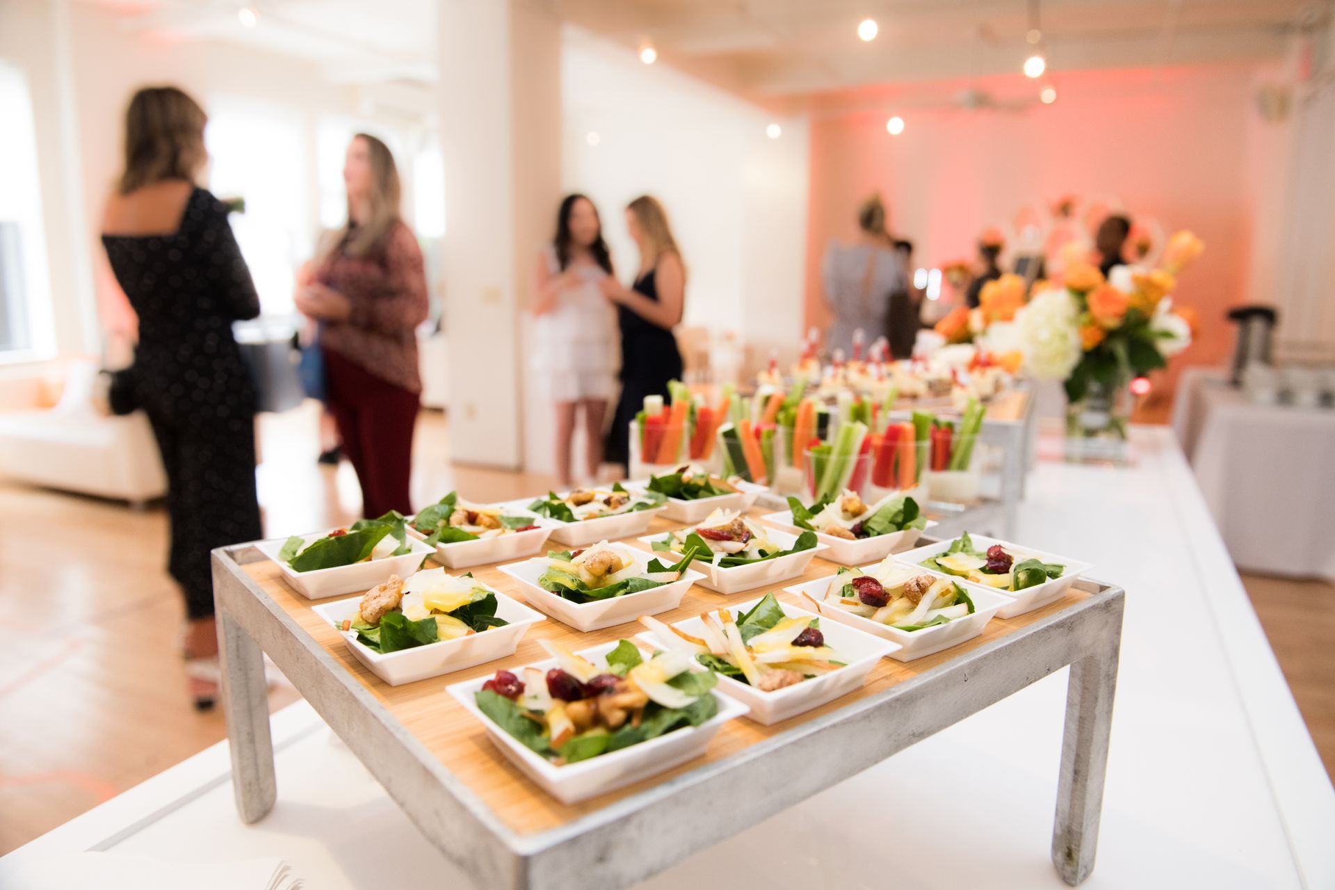 A buffet table with plates of food and people standing in the background.