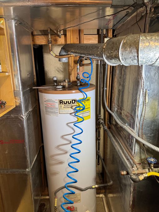 A water heater is sitting in a corner of a room next to a pipe.