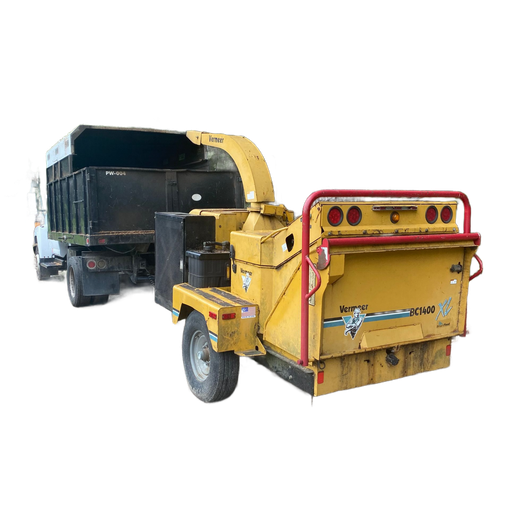 Yellow wood chipper connected to a truck, used for processing tree debris in a wooded area.