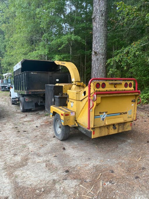 A yellow tree chipper is parked next to a dump truck.