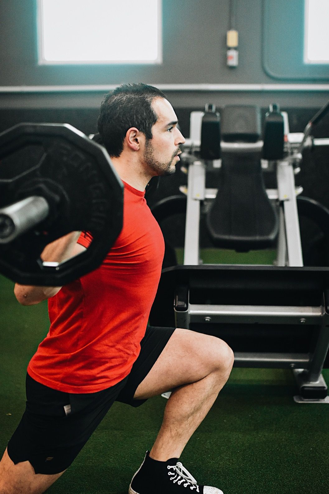 A man is squatting with a barbell over his head in a gym.