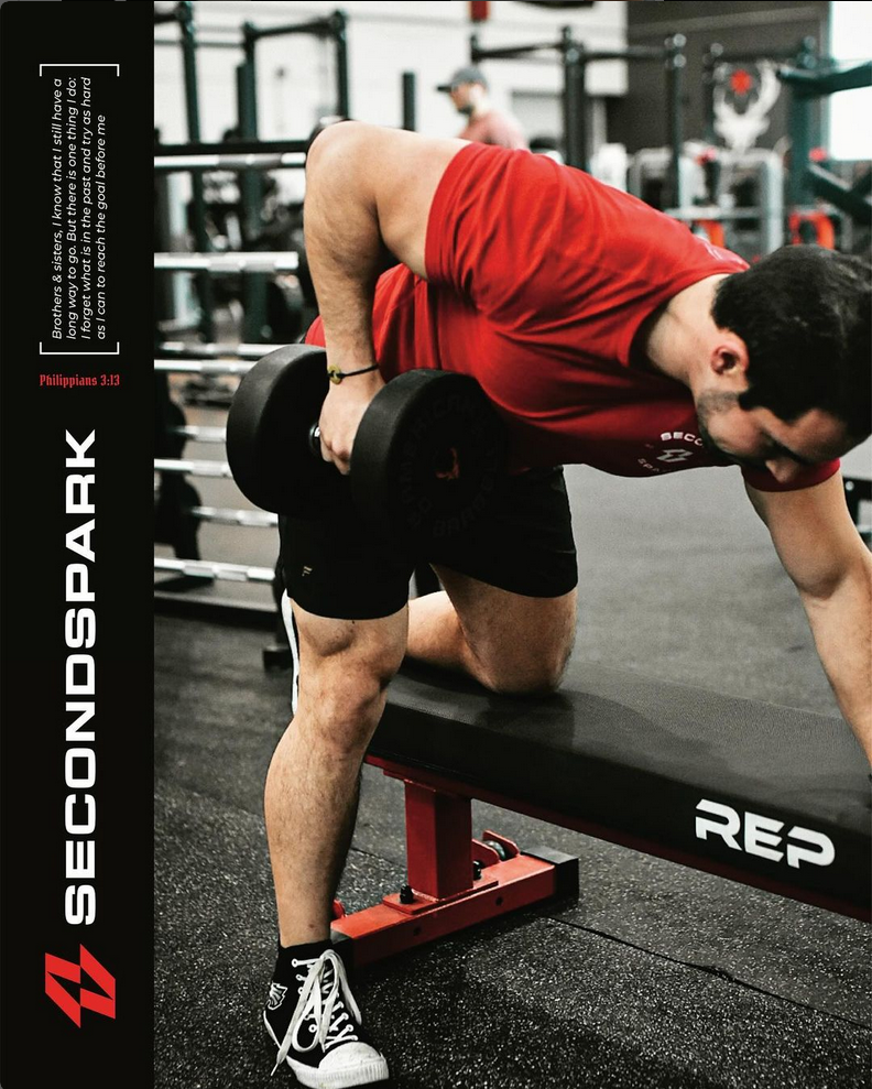 A man is lifting a dumbbell on a bench in a gym.