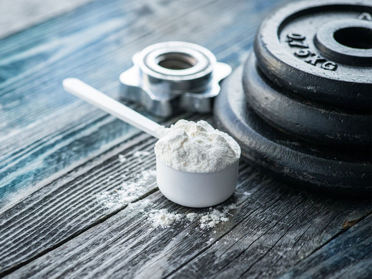 A scoop of protein powder next to a stack of dumbbells on a wooden table.